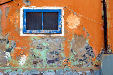 Blue framed window in weathered orange wall, old simple house wall in a Mediterranean location.