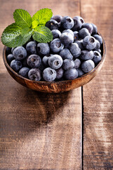 Bowl of fresh blueberries on rustic wooden board. Organic food blueberries and mint leaf for healthy lifestyle.