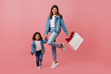 Mother and daughter in jeans holding hands. Studio shot of happy family posing on pink background.