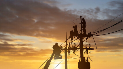 silhouetted electrician working on poles to install high-voltage equipment.