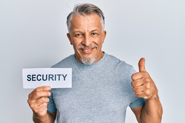 Middle age grey-haired man holding security word paper smiling happy and positive, thumb up doing excellent and approval sign