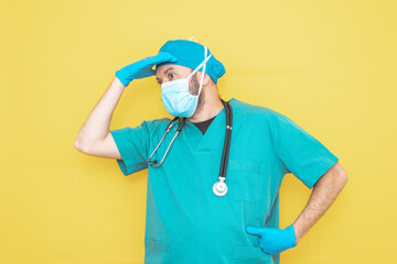 doctor dressed as a surgeon in green with stethoscope and mask on a yellow background with a worried expression.