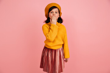 Preteen girl in knitted sweater sending air kiss. Studio shot of funny kid in yellow clothes.