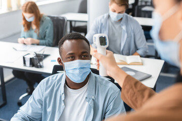 Obraz premium Teacher with contactless thermometer gun measuring temperature of black student