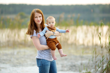 Little baby boy in his mothers arms. Mom and son having fun on sunny summer day in city park....