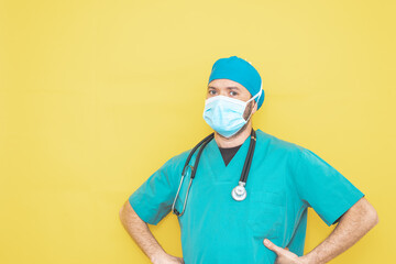 doctor dressed as a surgeon in green with stethoscope and mask on a yellow background with a worried expression.