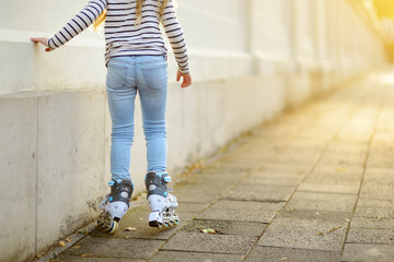 Young girl learning to roller skate on beautiful summer day on a street.