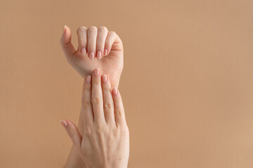 Hands of a beautiful well-groomed woman with feminine nails on a beige background. Manicure,...
