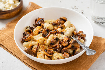 Gnocchi with mushrooms close-up. Cooked potato gnocchi with fried champignons and onions in a white plate on a light concrete table. Italian cuisine.