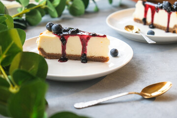 Vanilla classic cheesecake poured blueberries jam decorated fresh berries. Two plates of sweet cheesecake on table.