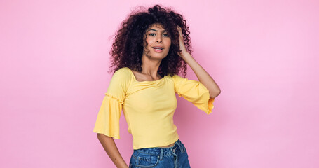 young model posing and adjusting curly hair isolated on pink