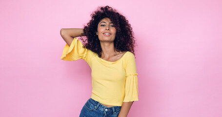 cheerful young model posing and adjusting curly hair on pink