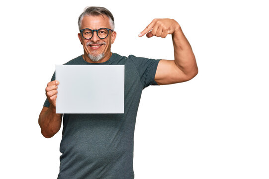 Middle age grey-haired man holding blank empty banner pointing finger to one self smiling happy and proud