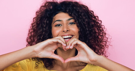 happy young woman showing heart sign with hands isolated on pink