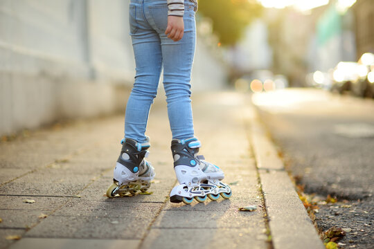 Young girl learning to roller skate on beautiful summer day on a street.