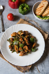 Popular Chinese delicacy chilli chicken prepared with green capsicum in a plate.