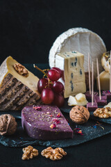 Variety of exclusive and colorful cheese, decorated with red grapes, on black background, vertical