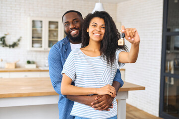 Hilarious African-American couple moved in the new house, cheerful beautiful woman in embraces of...