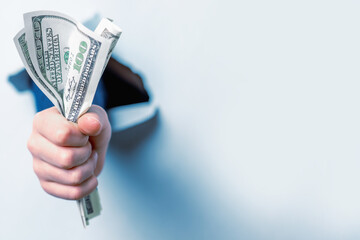Рand  full of US Dollar banknotes in fist punching through torn paper wall. Close up. Wealth, business, earnings, victory, domination, finance concept. Free copy space for design or text. © zwiebackesser