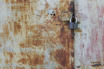A new padlock hangs from the old rusty metal doors of an abandoned garage or warehouse. Storage of old things