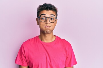 Young handsome african american man wearing glasses over pink background puffing cheeks with funny face. mouth inflated with air, crazy expression.