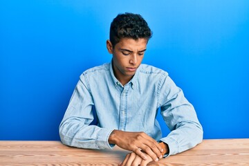 Young handsome african american man wearing casual clothes sitting on the table checking the time...