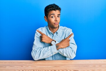 Young handsome african american man wearing casual clothes sitting on the table pointing to both sides with fingers, different direction disagree