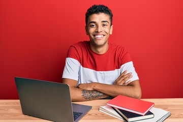 Young handsome african american man studying for school using laptop happy face smiling with crossed arms looking at the camera. positive person.