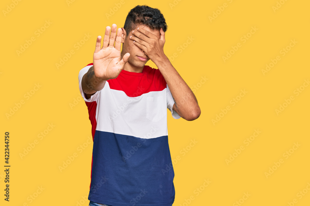 Sticker young handsome african american man wearing casual clothes covering eyes with hands and doing stop g