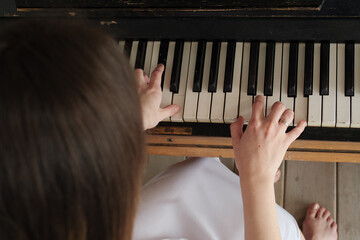 A woman in a white dress and barefoot plays the piano in the studio. Concept of art and love for music, pleasure of classical music