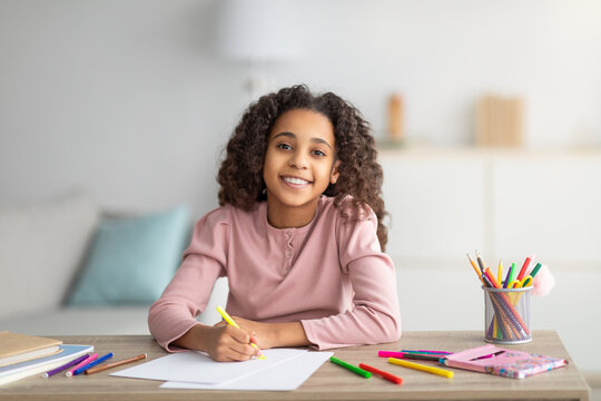 Happy black schoolgirl drawing picture at home