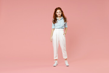 Full length body of young student positive smiling happy caucasian european redhead woman 20s wearing blue shirt pants standing looking camera isolated on pastel pink color background studio portrait.
