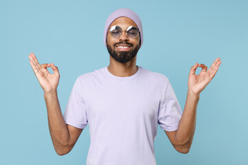 Young smiling spiritual unshaven black african man in violet t-shirt hat glasses hold spread hands...