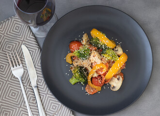 Delicious salad made of broccoli, cherry tomatoes, yellow pepper, mushrooms, pieces of chicken breast and sesame seeds with glass of wine on the table. Healthy food for dinner or lunch.