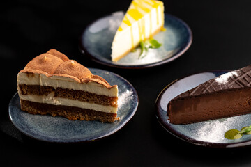A few different desserts, assorted sweets on plates on a black background. Vanilla classic and chocolate cake, carrot cake.