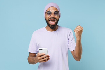 Young unshaven student black african man 20s in violet t-shirt purple hat glasses using mobile cell...
