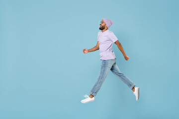 Obraz premium Full length side view of young confident excited happy unshaven black african man in violet t-shirt hat glasses jump high walk in air going isolated on pastel blue color background studio portrait.