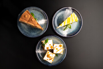 A few different desserts, assorted sweets on plates on a black background. Vanilla classic and chocolate cake, carrot cake.