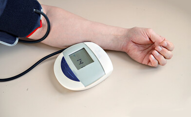Tonometer measures blood pressure in man. Hand with device is on gray table