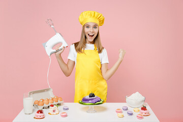 Teen girl chef cook confectioner baker in yellow apron toque cap at table hold kitchen mixer do...