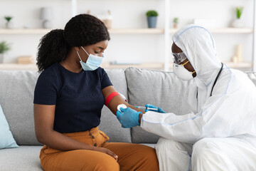 Doctor in protective suit taking blood sample for female patient - obrazy, fototapety, plakaty
