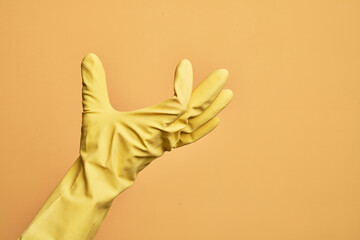 Hand of caucasian young man with cleaning glove over isolated yellow background picking and taking...