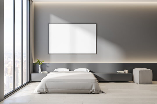 Blank white poster in black picture frame on grey wall in sunny bedroom with cozy bed and city view from big window. Mock up