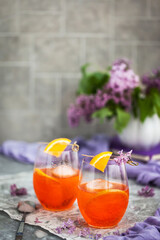 Orange Aperol Spritz cocktail served in a wine glasses, decorated with slice of orange and lilac