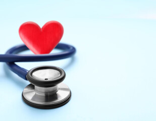 Stethoscope and red heart on light blue background, space for text