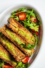 Grilled avocado and cheese sandwiches with fresh salad in white dish, top view. Healthy snack concept.