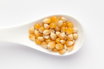 Macro Close up organic yellow corn seed or maize (Zea mays) on a white ceramic soup spoon. Top view