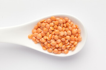 Macro Close-up of Organic masoor dal (Lens culinaris) or whole pink dal on a white ceramic soup spoon. Top view