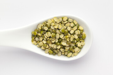 macro Close-up of Organic green Gram (Vigna radiata) or spilt green moong dal unpolished on a white ceramic soup spoon. Top view