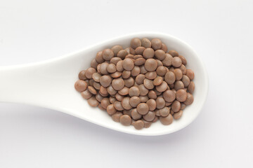 Macro Close up of Organic masoor dal (Lens culinaris) or whole brown dal on a white ceramic soup spoon. Top view